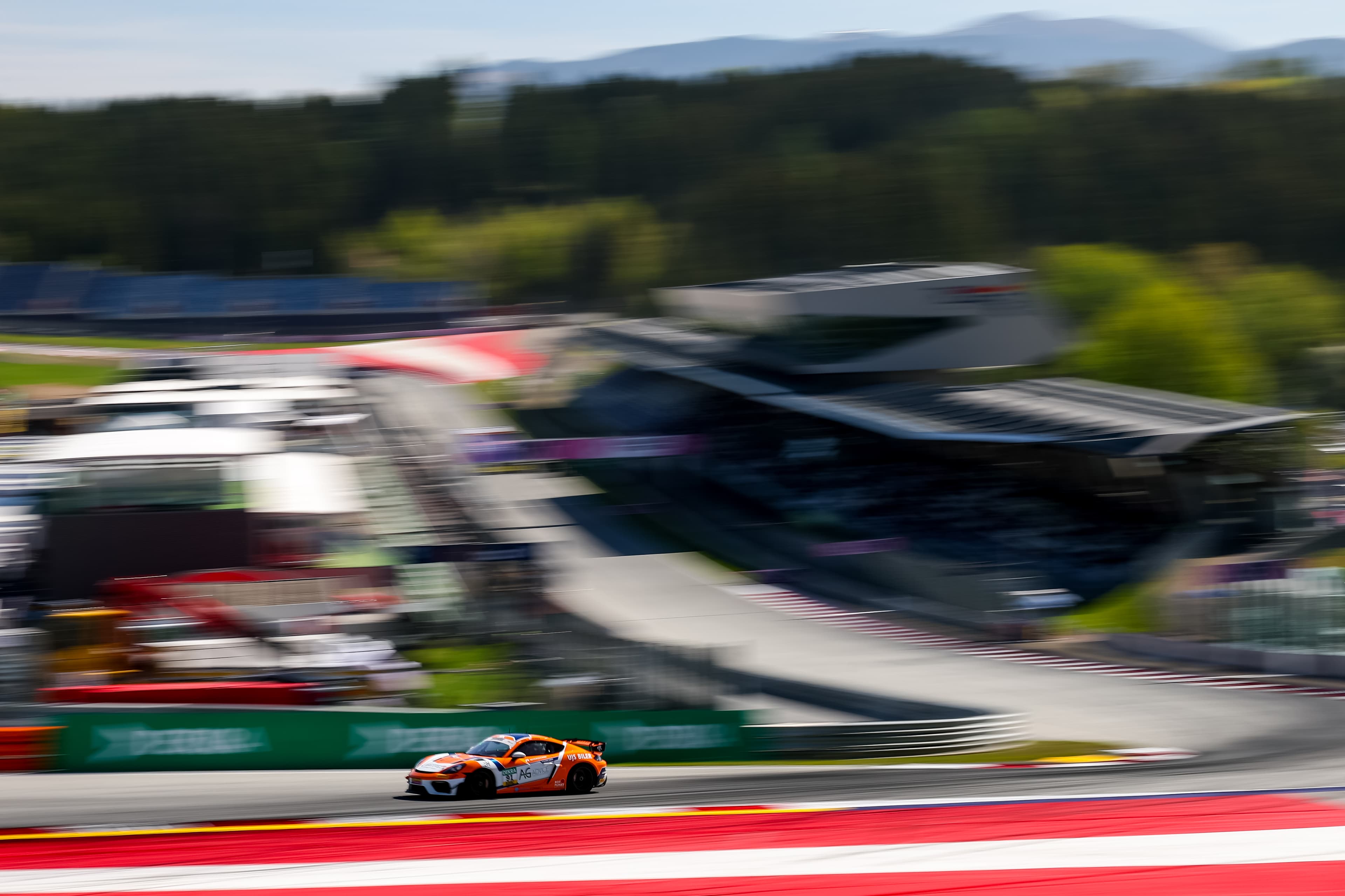 The #91 Porsche 718 Cayman GT4 RS sharp against the motion-blurred Red Bull Ring grandstands, 2026